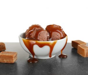 Bowl with chocolate ice cream and caramel sauce on table